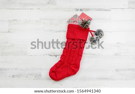 Chunky  knit red Christmas stocking with pom pons on a white wooden background with space for copy