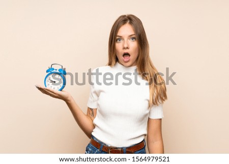 Young blonde woman over isolated background holding vintage alarm clock