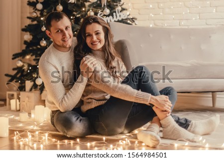  Beautiful young couple sitting on the floor and celebrating new year in front of Christmas tree.