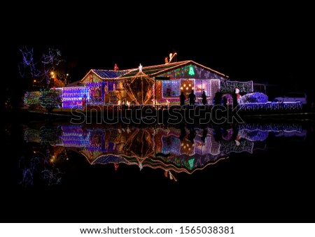 Depicts a regional Christmas light decoration award winning house with light display reflected in still water. Enhances the spirit of Christmas.