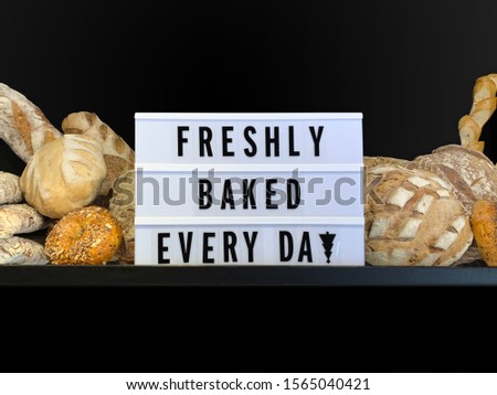 Variety of bread loaves with sign reading "Freshly baked every day" in black letters  on cinema light box. Dark black background with space for text or copy
