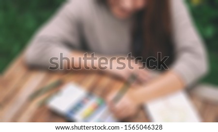 Blurry background of a young beautiful woman drawing and painting with water color at outdoor