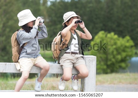 Two asia little girl carrying a backpack and wearing a hat. Use binoculars and take pictures Children enjoy the surrounding nature. She enjoys traveling in the summer. travel and adventure concept.