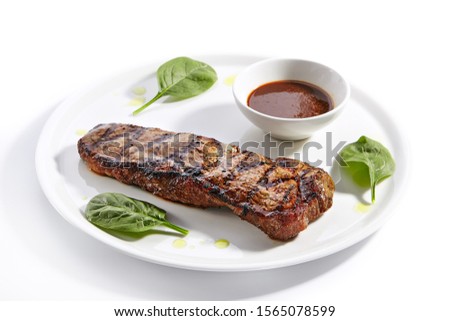 Striploin steak with sauce close up. Grilled beef with basil leaves isolated on white background. Barbeque meat, roasted pork served on plate composition. Traditional New York strip steak