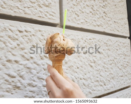 a hand holding a gelato in front of a tile wall
