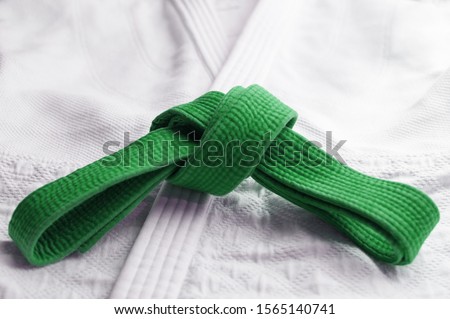 Green martial art belt tied in a knot on white gi in background Royalty-Free Stock Photo #1565140741