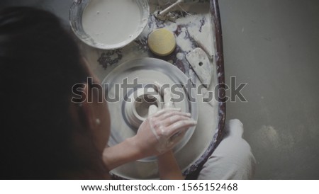 Top down shot of dark haired female master potter molds clay pot at pottery wheel. Woman works in pottery workshop