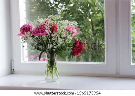 Bouquet of  pink and rad peony in a simple glass vase near window used for interior decoration 