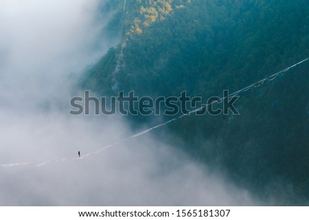 a man walks along a stretched sling high above the clouds. highliner catches the balance on a long and high sling pull in a canyon. Extreme sports in Bosnia and Herzagovina,
