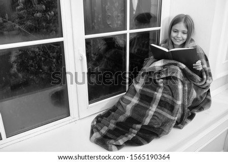Magic xmas spirit. Little girl enjoy reading Christmas story. Little child read book on Christmas eve. Little reader wrapped in plaid sit on window sill. Childrens picture book. Winter wonderland.