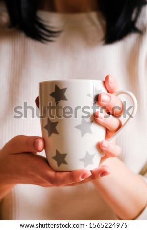 The girl in a cozy clothes drinking coffee froma a mug. hands holding hot cup of coffee or tea in morning. cup in female hands