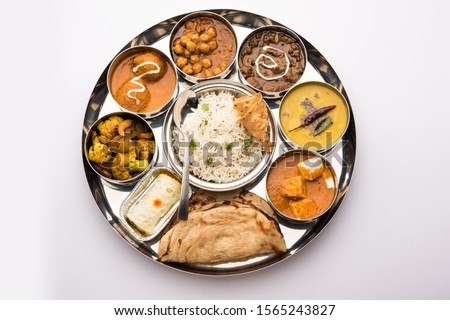 Indian vegetarian Food Thali or platter includes paneer butter masala, dal makhani / tarka, chole papad, kofta curry, gulab jamun, aloo-gobi sabji, chapati and rice with Bengali sweet served Royalty-Free Stock Photo #1565243827