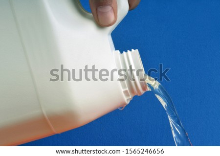 Pour bleach in closeup on blue background Royalty-Free Stock Photo #1565246656