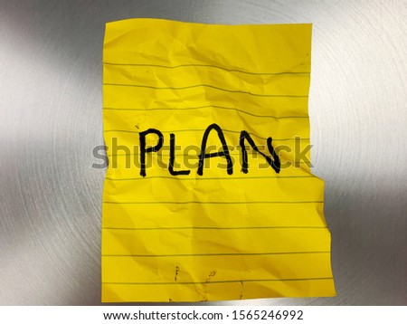 The word "plan" on a crumpled yellow sticky note and silver background.