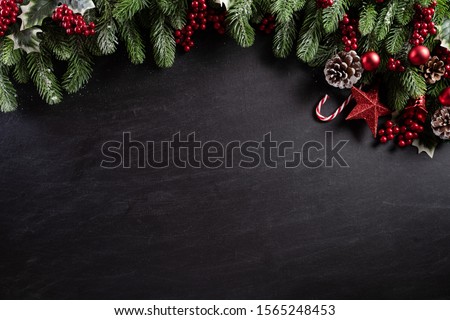 Christmas background concept. Top view of Christmas gift box red balls with spruce branches, pine cones, red berries and bell on black wooden background.