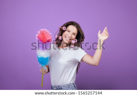 A housewife in pink curlers holds a dust brush in her hands, laughs and dances while cleaning. Funny cleaning. Cleanliness and tidiness.