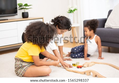 Mom and Children in living room kids playing troy together on floor while young mom relaxing at home on sofa, little boy girl having fun, friendship between siblings, family leisure time in living 