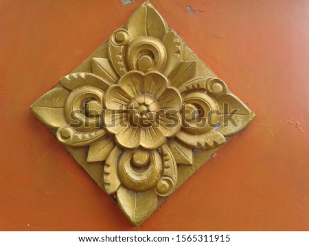 Wall decoration made of a mixture of cement and sand in the form of carved floral motifs to beautify the outer walls of the house. Gold wall hangings mounted on the walls of the house are orange.