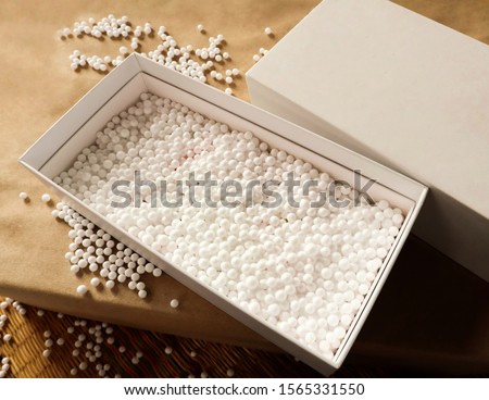 A white square gift box placed on a paper floor with decorative foam beads for beauty.