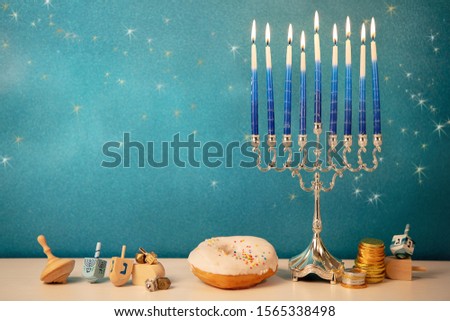 concept of of jewish religious holiday hanukkah with glittering raditional chandelier menorah, spinning top toys (dreidel), a doughnut and chocolate coins