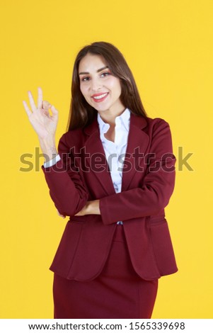 Beautiful woman in red dress showing right fingers OK symbol and gesture isolated on yellow background - working and business woman concept 
