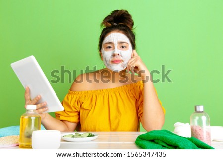 Portrait of young caucasian woman in beauty day, skin and hair care routine. Female model making selfie, vlog or videocall while applying facial mask. Selfcare, natural beauty and cosmetics concept.