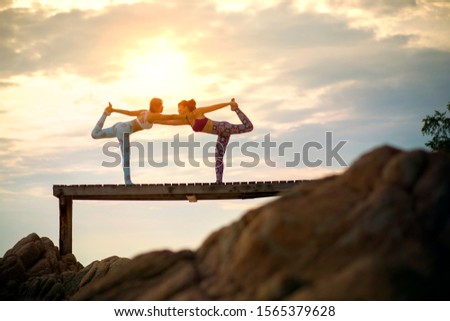 couples of woman playing yoga pose on beach pier with moring sun light 