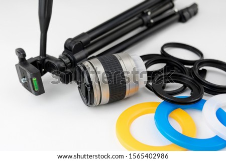 Small tripod, camera lens, color filters and adapter rings on white background
