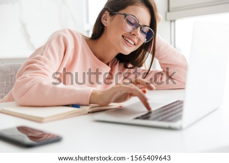 Smiling prettty girl working on laptop computer while sitting at the kitchen table