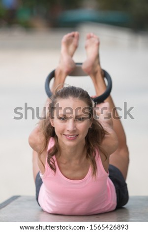 Pilates teacher with a slim athletic body and beautiful face, working out with a Pilates ring in an urban skate park.
