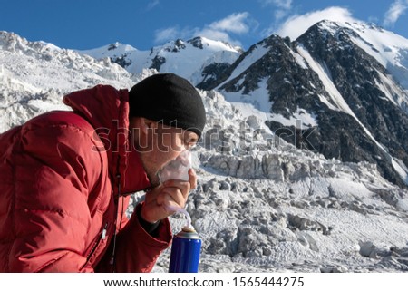 High altitude sickness. Climber breathing oxygen from the O2 tank on the background of glacier and covered with snow and ice mountains. Royalty-Free Stock Photo #1565444275