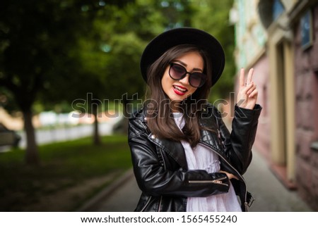 Happy young woman taking selfie with peace sign on city street.