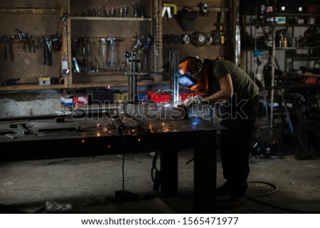 A male welder in a protective helmet works in his workshop. Welding process