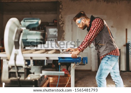 Young man work in home workshop using laptop and reads the manual