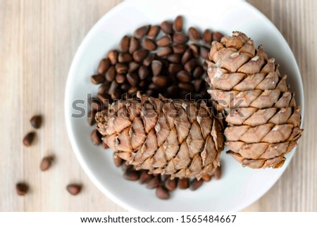 Pine cones and nuts on white plate on natural light whitewashed wooden background. Healthy eating organic food, vegetarian concept. Top view. Selective soft focus. Shallow depth of field. Copy space