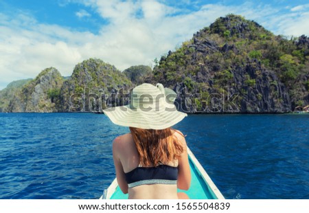 a woman in a beach hat on the bow of the boat, in the background a paradise lagoon Royalty-Free Stock Photo #1565504839
