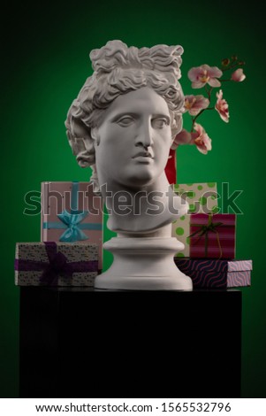 White plaster Statue of Apollo Belvedere, flowers and gifts boxes and packages, spotlights and multi-colored backgrounds. Composition for congratulations, background for design.