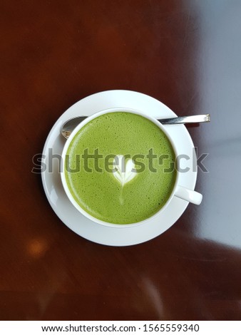 Picture of delicious macha latte coffee placed in a white coffee cup on a brown table