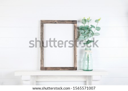Mock up of a rough wooden frame on a white wall background in the interior - empty mock up frame with eucalyptus branches