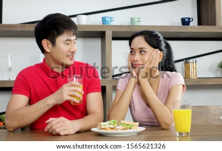 Portrait of cute happy couple in cheerful action proudly presenting with happiness to audience the breakfast  decorated with ingredient of sandwich and  orange juice in modern kitchen.