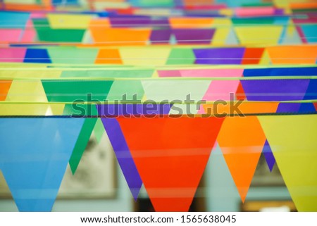 Garland of triangular multi-colored holiday flags. Charity fair or anniversary celebration. Selective focus. Indoors