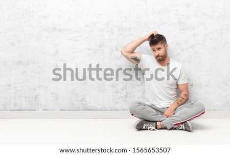 young handosme man feeling puzzled and confused, scratching head and looking to the side against flat color wall