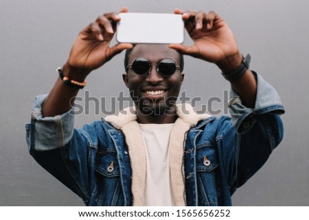 Portrait of happy smiling african man taking selfie picture by smartphone on gray wall background