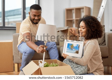 moving, people, repair and real estate concept - happy african american couple packing stuff into cardboard boxes at home