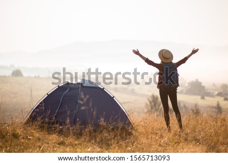 Successful hiking woman silhouette on top of mountains, motivation and inspiration in beautiful sunset view. Female hiker with arms up outstretched on mountain top, inspirational landscape. Camping