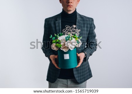 A young guy in the image of a teacher holds a box of flowers.
Translation of the text on the wooden plate "Happy Teacher's Day."