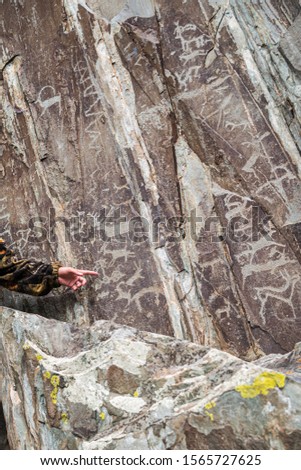 Guide hand pointing to petroglyphs on a rock. Photo taken at the Adyr-Kan shrine in the Altai mountains