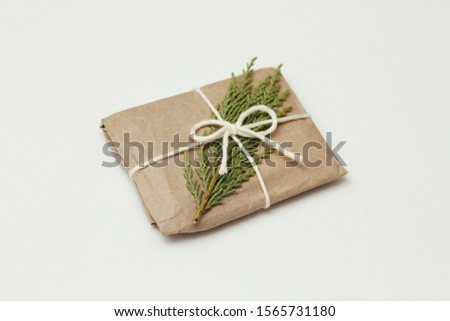 Gift box wrapped in brown craft paper and tie white thread. Christmas mood. White solid background. Present package. Coniferous twig.
