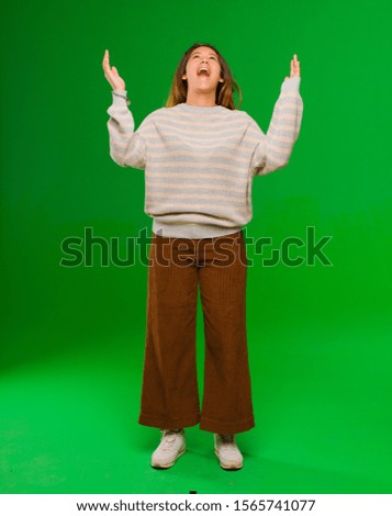young pretty latin woman feeling happy, amazed, lucky and surprised, celebrating victory with both hands up in the air against green wall