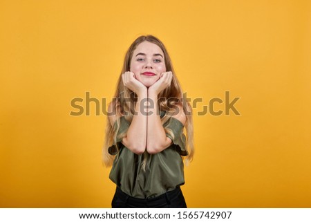 Portrait of confused young woman looking directly and covering chin with hand isolated on orange wall background in studio. People sincere emotions, lifestyle concept.
